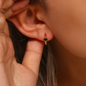 Close-up of a gold huggie hoop earring with a sparkling green round zircon stone on an ear