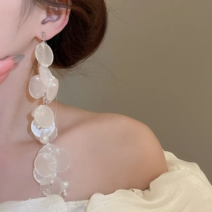 Detailed view of long shell and pearl tassel earrings on a model with warm lighting