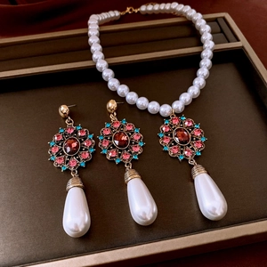 Detailed close-up of retro pearl necklace and earrings set with red gems and blue diamonds