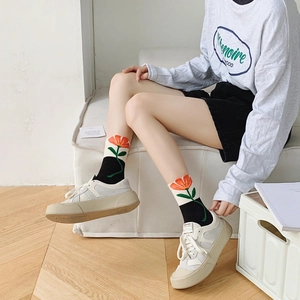 Detail of mid-calf black socks featuring bright orange tulip floral pattern and green leaves
