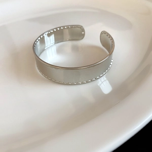 Detaillierte Nahaufnahme eines silbernen Metallarmreifs mit edlem Wellenrand-Design