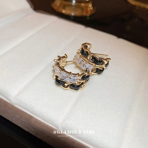 Close-up of C-shaped chain earrings with black weaving and square cubic zirconia