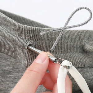 Flexible metal drawstring threader tool guiding a white cord through grey garment waistline