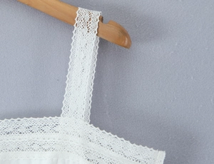 Close-up of intricate white lace pattern on dress hanging on a wooden hanger