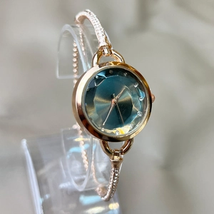 Close-up of gold ladies watch featuring a faceted teal dial and diamond-set slim bracelet