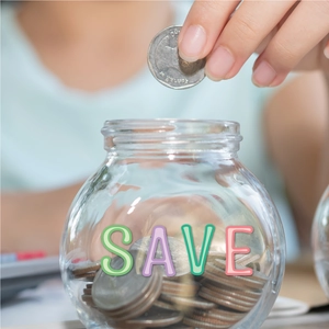 Close-up of a hand placing coins into a glass savings jar with Save lettering