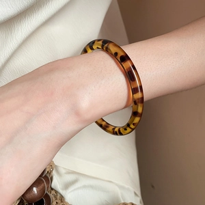 Close-up of a vintage tortoiseshell resin bangle on a model wrist against white fabric