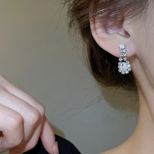 Close-up of silver teardrop earrings with crystals worn by a model in soft lighting