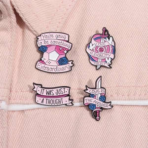 Détail de broches en émail rose avec épées et gemmes sur du tissu denim rose