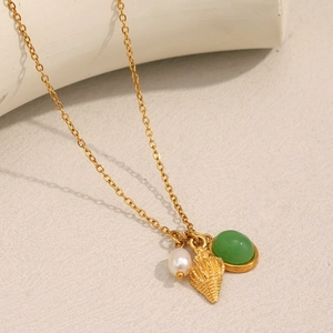 Detail of 18K gold necklace featuring a white pearl, sea shell, and green gemstone