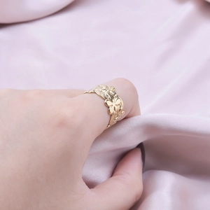 Adjustable golden stainless steel flower ring shown on a model with pink silk background