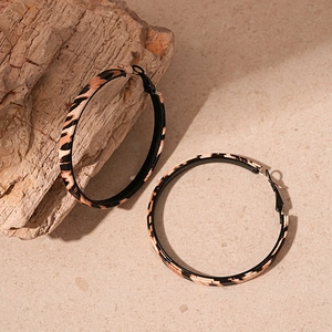 Macro view of geometric leopard print leather hoop earrings on a stone surface