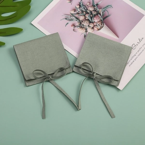 Two sage green microfiber jewelry pouches with ribbon ties on a floral garden backdrop