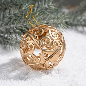 Detail of a golden hollow Christmas ball with floral patterns on snowy background