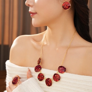 Detail of red enamel jewelry set with gold necklace, earrings and ring worn by model