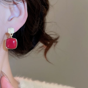 Close-up of red enamel square drop earrings with textured gold studs on model