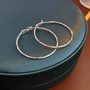 Macro detail of large silver hoop earrings with hammered texture on a leather jewelry box