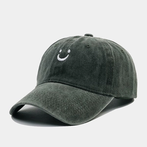 Close-up of white smiling face embroidery on washed charcoal grey cotton baseball cap