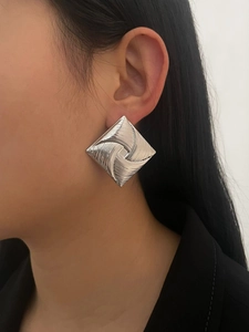 Close-up of geometric silver square earring with embossed swirl texture on model
