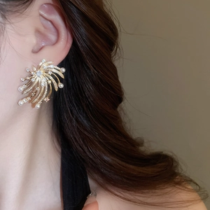 Close-up of golden starburst earrings with pearls and crystals worn by a model