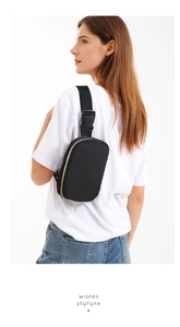 Detail of black nylon crossbody bag on model with gold zippers and adjustable strap
