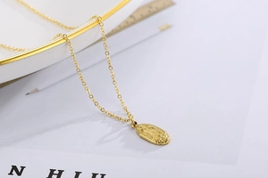 Détail macro du collier avec pendentif ovale Vierge Marie doré sur une assiette blanche