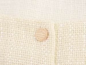 Vue macro du tissu en tweed crème aux fils dorés et bouton doré texturé élégant