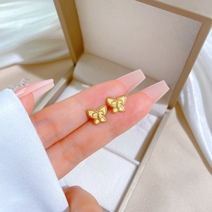Minimalist vintage butterfly stud earrings in gold titanium steel held against silk background