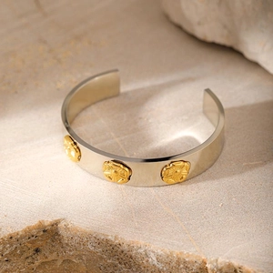 Minimalist silver stainless steel open bangle with golden flower accents on a stone