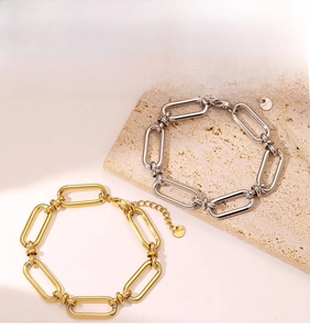 Detail of gold and silver chain bracelets with oval links and logo tags on stone