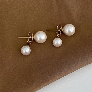 Detail of elegant gold double pearl drop earrings on smooth brown silk fabric