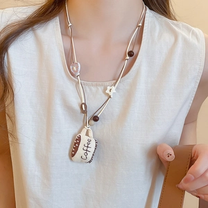 Detail of coffee cup fabric pendant necklace with heart bead on a cream sweater
