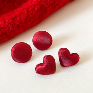 Dettaglio ravvicinato di orecchini in tessuto rosso a cuore e tondi con trama in seta