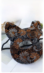 Detailed macro view of black fabric cat mask with orange and silver sequin flower patterns
