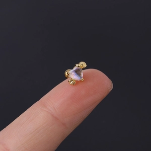 Macro view of tiny gold heart wing ear stud with iridescent stone on a fingertip