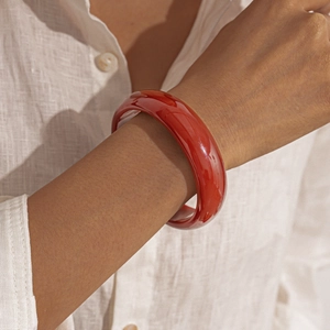 Close-up of a smooth red resin geometric bangle worn on a wrist with a linen shirt
