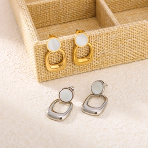 Gold and silver stainless steel earrings with cat eye stone pendants on a beige display