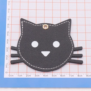 Close-up of black leather cat keychain with white stitching on a blue grid mat