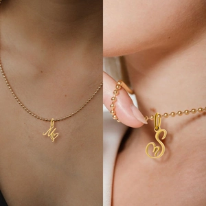 Close-up of golden cursive initial pendant with heart detail on a delicate bead chain