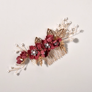 Détail d'un peigne de mariée avec fleurs en tissu rouge foncé et feuilles dorées