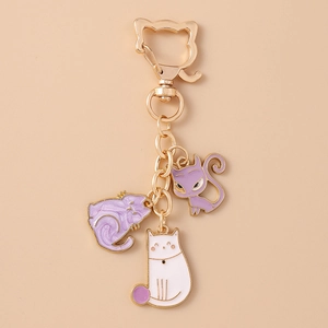 Close-up of golden keychain with three cute purple and white enamel cat charms