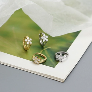 Detail view of gold and silver S925 flower earrings with zircons on a magazine