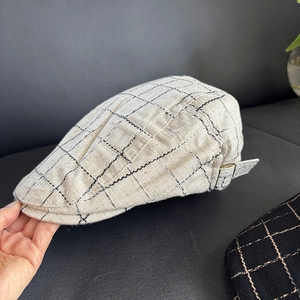Detail of light beige plaid flat cap featuring adjustable metal buckle and linen texture