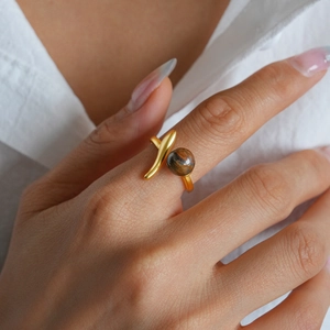 Close-up of golden asymmetric ring with round brown tiger eye stone on finger