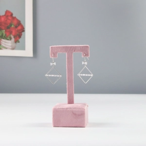 Close-up of silver geometric square earrings with bow detail on pink velvet stand