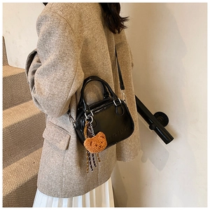 Detail of black glossy handbag with meiya embossing and a cute brown plush bear charm
