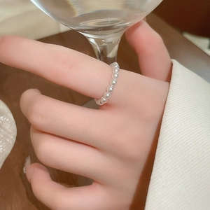 Close-up of white beaded pearl elastic ring worn by a model holding a wine glass