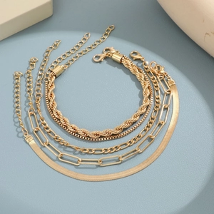 Detail view of five different golden chain bracelets on a light blue background