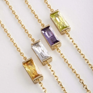 Detail of four gold necklaces featuring rectangular gemstones in yellow, white, purple and green