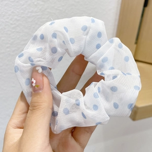 Detail of white mesh hair scrunchie with blue polka dots held by hand for soft texture